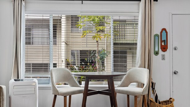 Une pièce avec une fenêtre, deux chaises, une table, un radiateur et une porte.