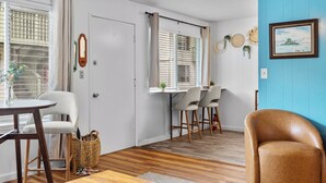 Une pièce avec un plancher en bois, un coin repas comprenant des chaises et une table, ainsi qu’une fenêtre avec des stores.