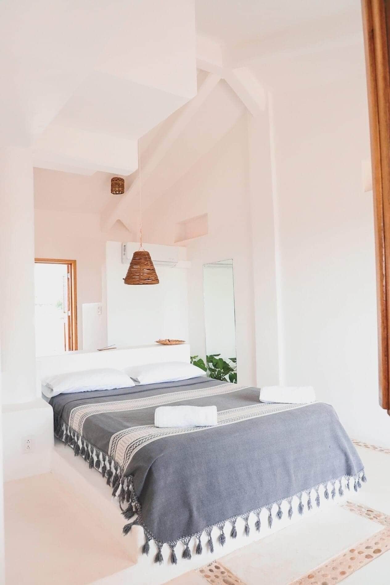 A spacious bedroom with a large bed, a hanging light fixture, and a view of the outside.
