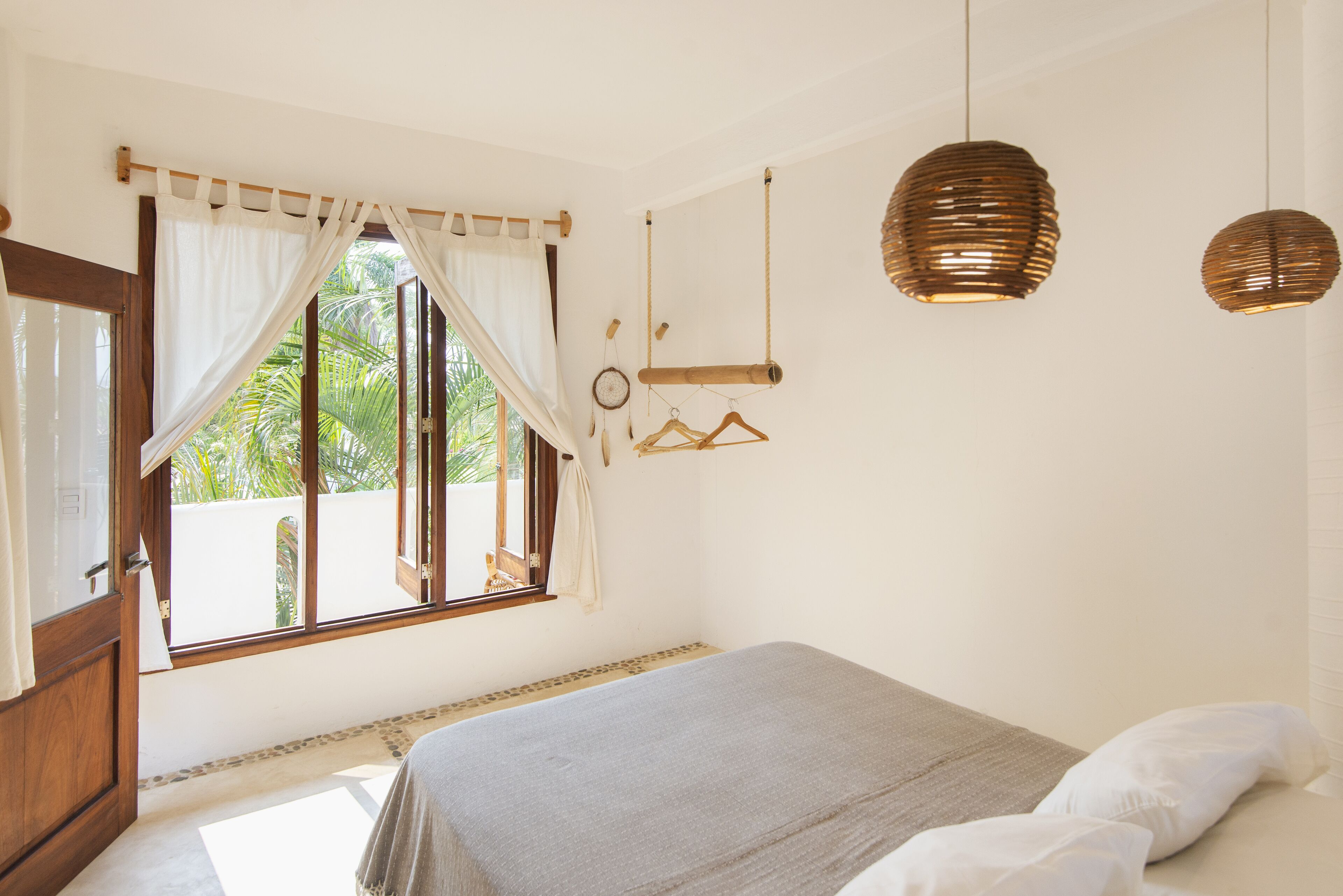 A bedroom with a bed, a window with curtains, a hanging light fixture, and a view of greenery outside.