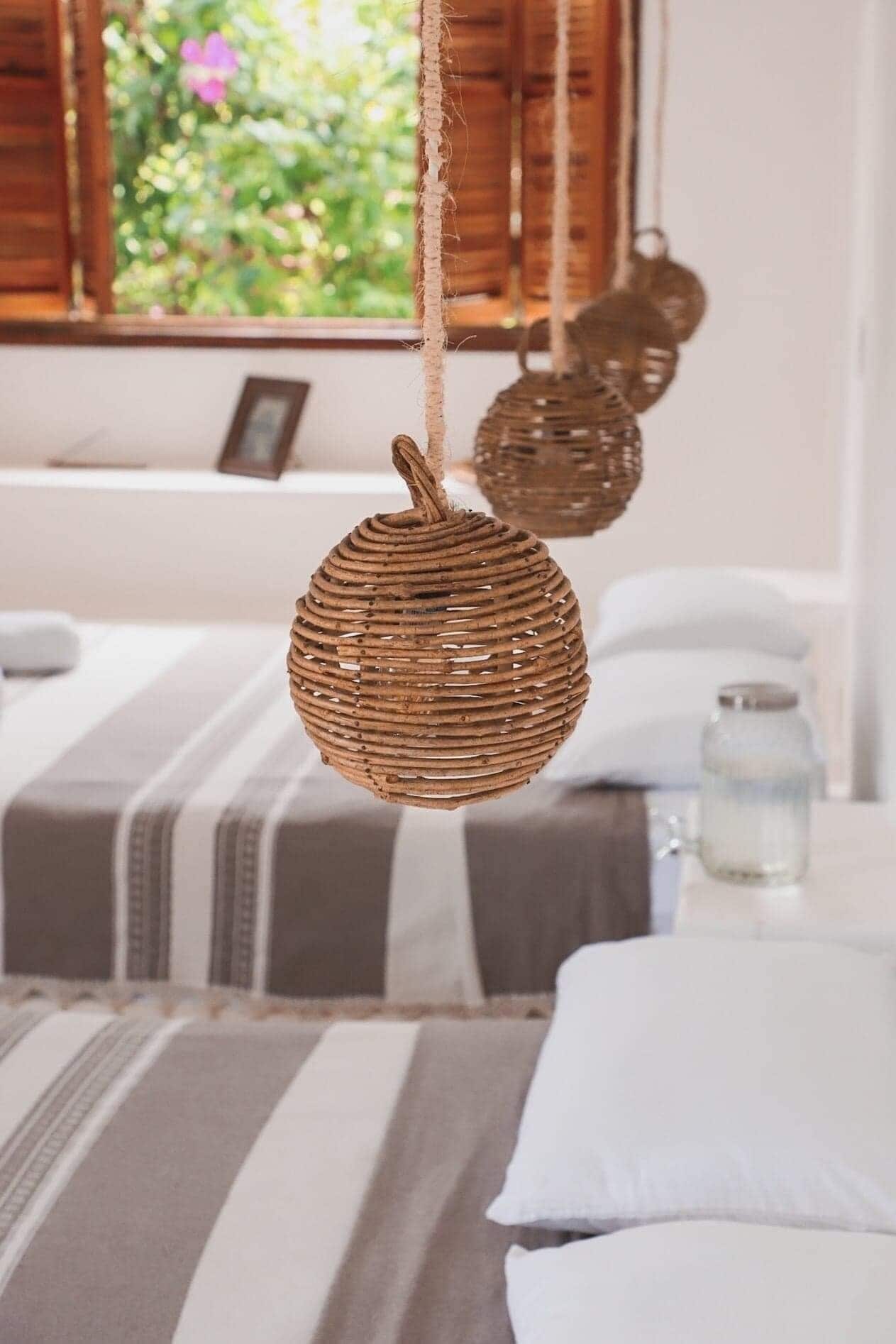 A bedroom with striped bedding, a hanging woven basket, and a window with a view of greenery.