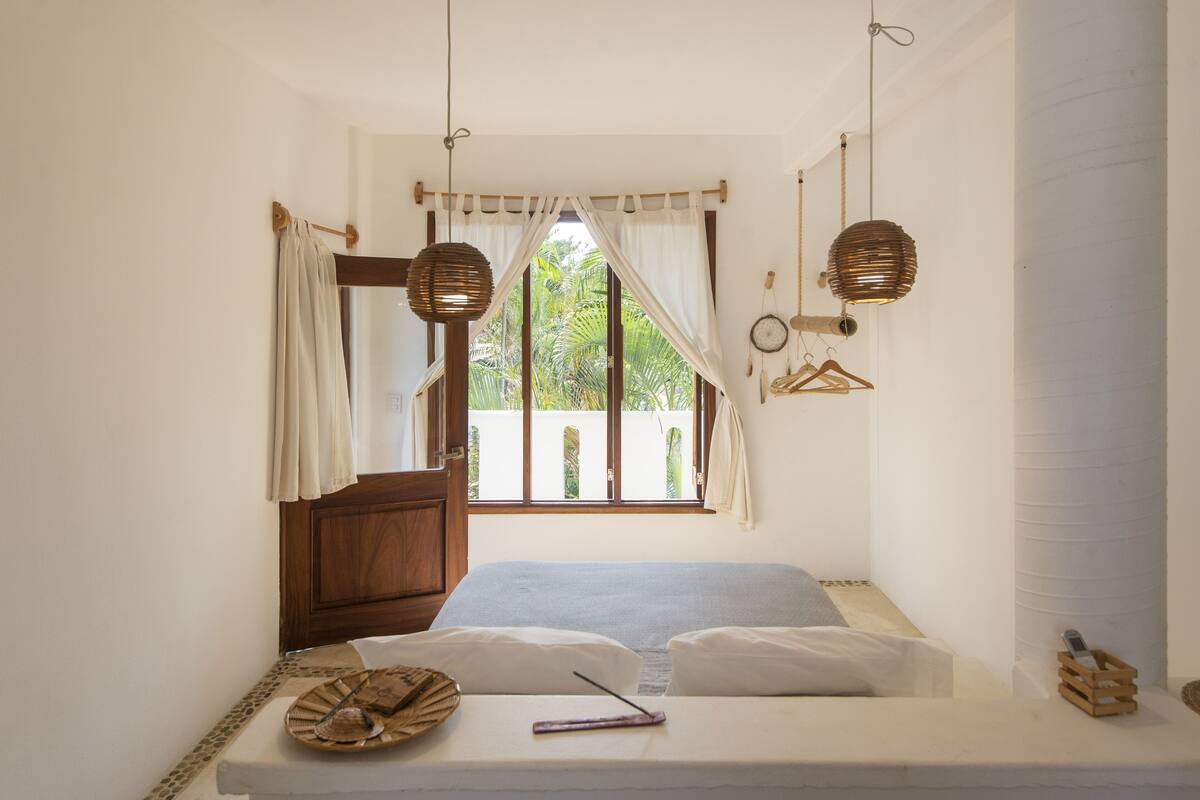 A bedroom with a bed, curtains, a window with a view, and hanging lamps.