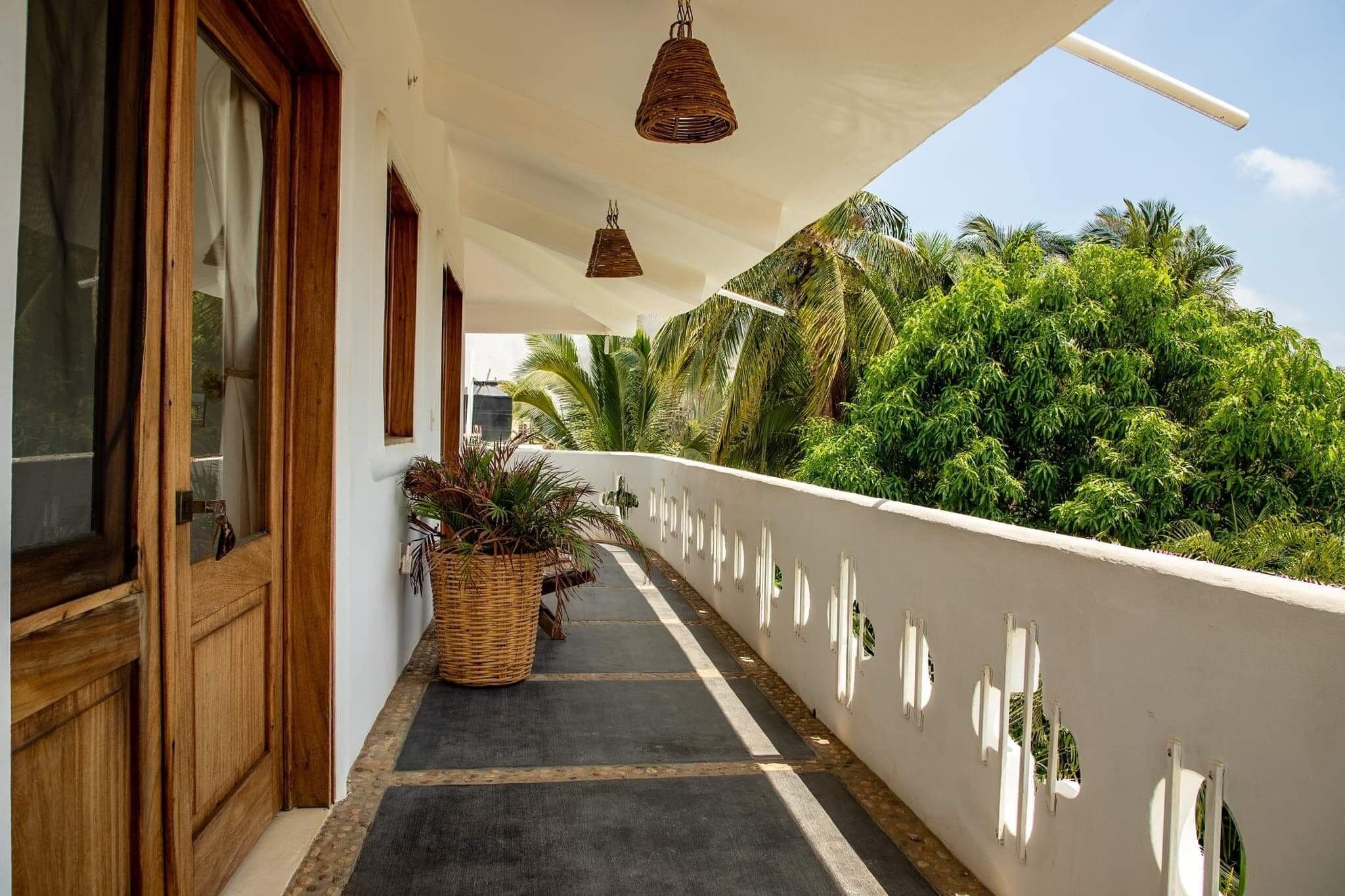 A balcony with a white railing, potted plants, and hanging wicker lamps.