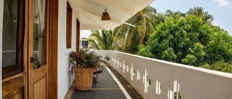 A balcony with a white railing, potted plants, and hanging wicker lamps.