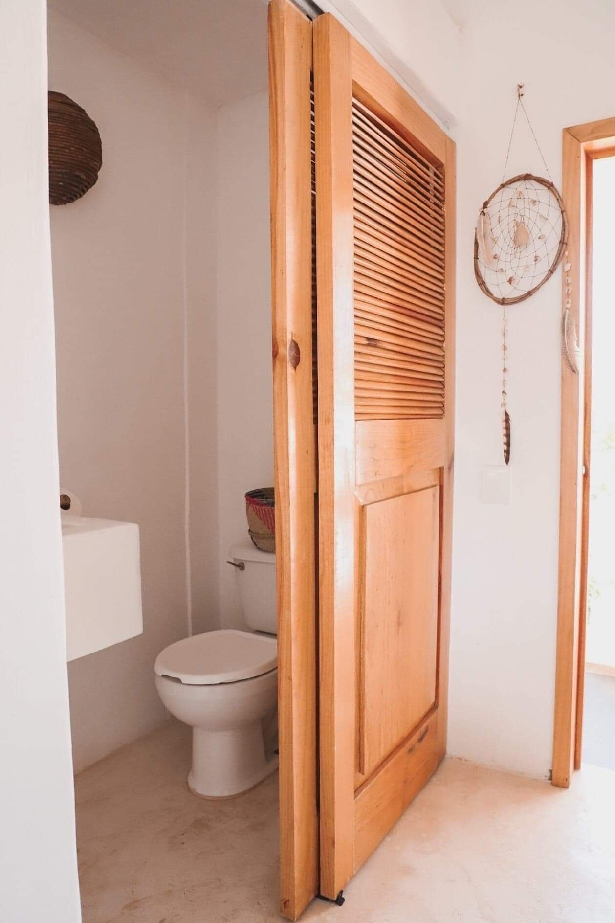 A bathroom with a wooden door, a toilet, and a dreamcatcher on the wall.