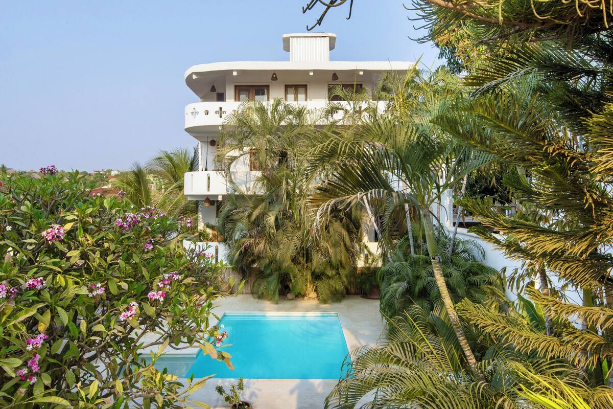 A modern building with a pool surrounded by lush greenery and palm trees.