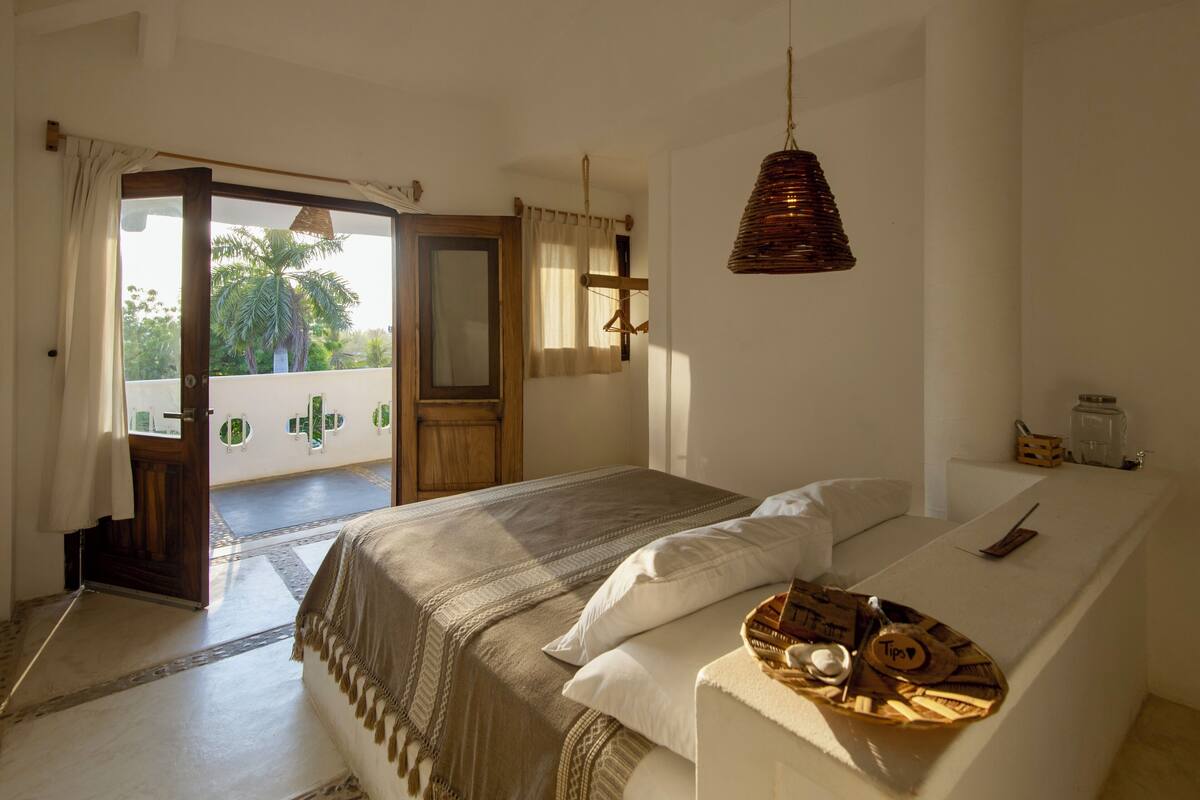 A bedroom with a bed, a bedside table, a hanging lamp, and a view of the outdoors.