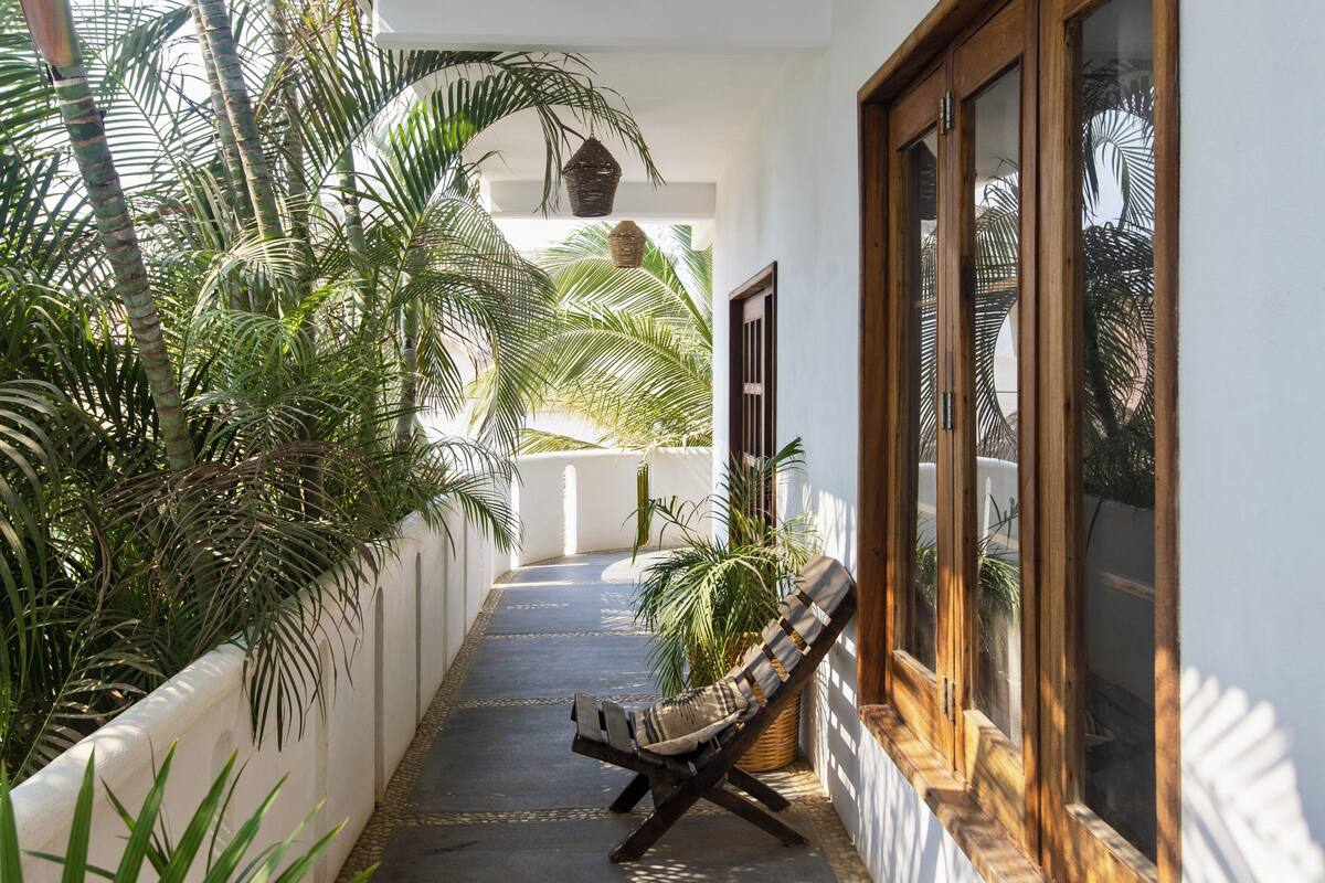 A narrow corridor with a cushioned chair, potted plants, and a window with wooden frames.