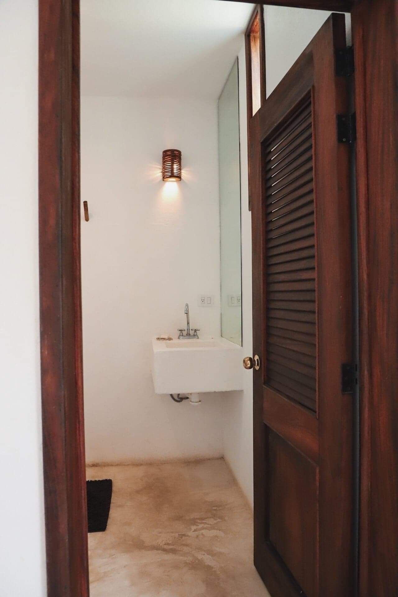 A narrow bathroom with a white sink, a mirror, and a wooden door.