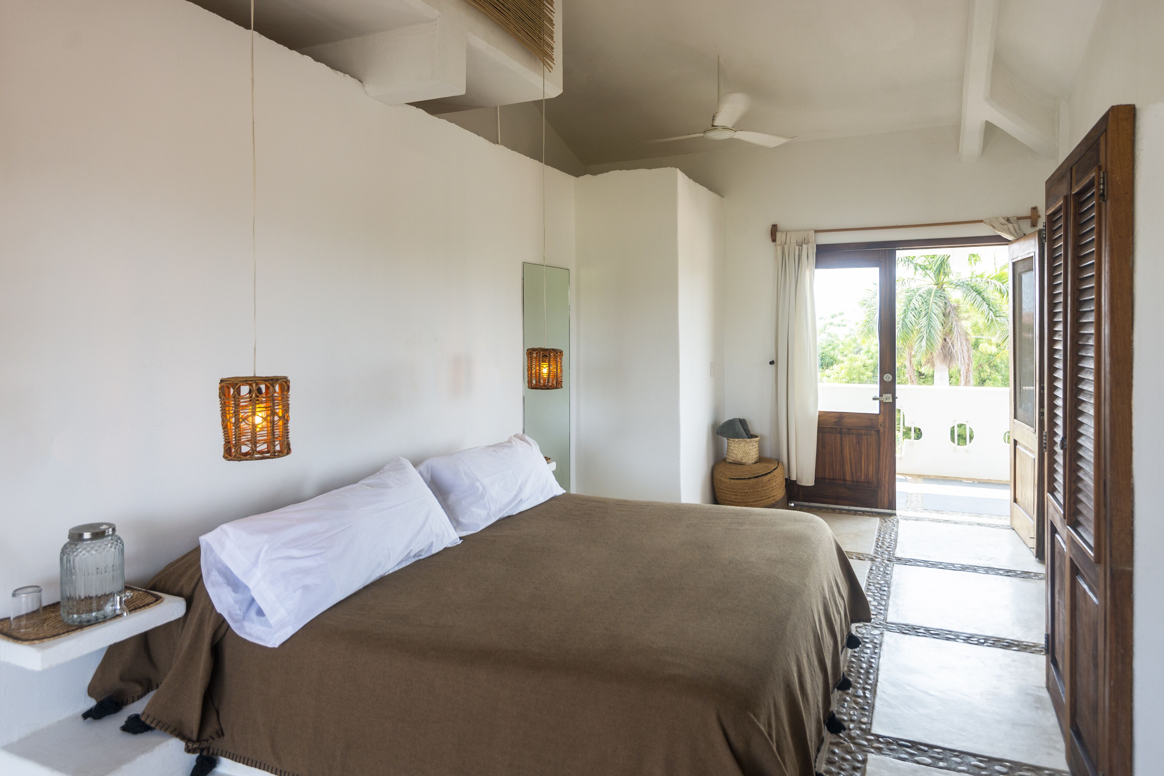 A bedroom with a bed, bedside tables, a mirror, and a door leading to a balcony.