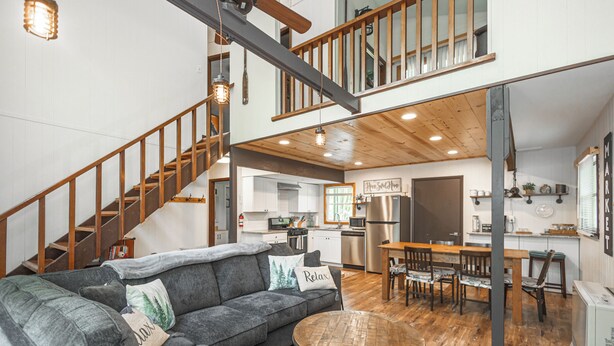 A spacious living area with a gray sectional sofa, a round wooden coffee table, and a staircase leading to an upper level.