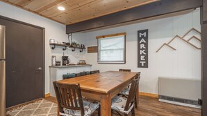 A dining area with a wooden table and chairs, a kitchen with white cabinets, and a wall-mounted sign that reads "MARKET".
