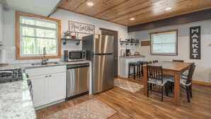 A modern kitchen with white cabinets, stainless steel appliances, wooden flooring, and a dining area with a wooden table and chairs.
