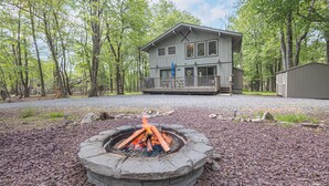 A lodge with a fire pit in the foreground, surrounded by a gravel area and trees.