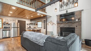 A modern kitchen with a built-in oven, a dining area with a wooden table and chairs, and a cozy living room with a gray sofa.