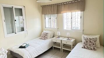 Un dormitorio con dos camas individuales, una mesita pequeña, una lámpara y una ventana con cortina.