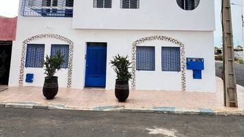 Un edificio blanco con varias ventanas, una puerta azul y dos grandes macetas con plantas en la acera.
