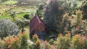 A wooden cabin with a red roof surrounded by lush greenery and trees. - Hostal La Laguna (Villamaria)