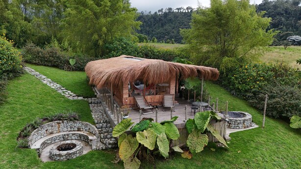 A thatched-roof hut with a stone fire pit, surrounded by lush greenery and a stone pathway. - Hostal La Laguna (Villamaria)
