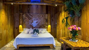 A wooden room with a bed, two wall-mounted lights, a wooden table with a vase of flowers, and a wooden ceiling. - Hostal La Laguna (Villamaria)