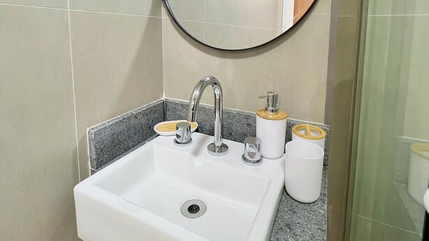 A bathroom with a white sink, chrome faucet, and a round mirror. - Brera Moema NR (São Paulo)