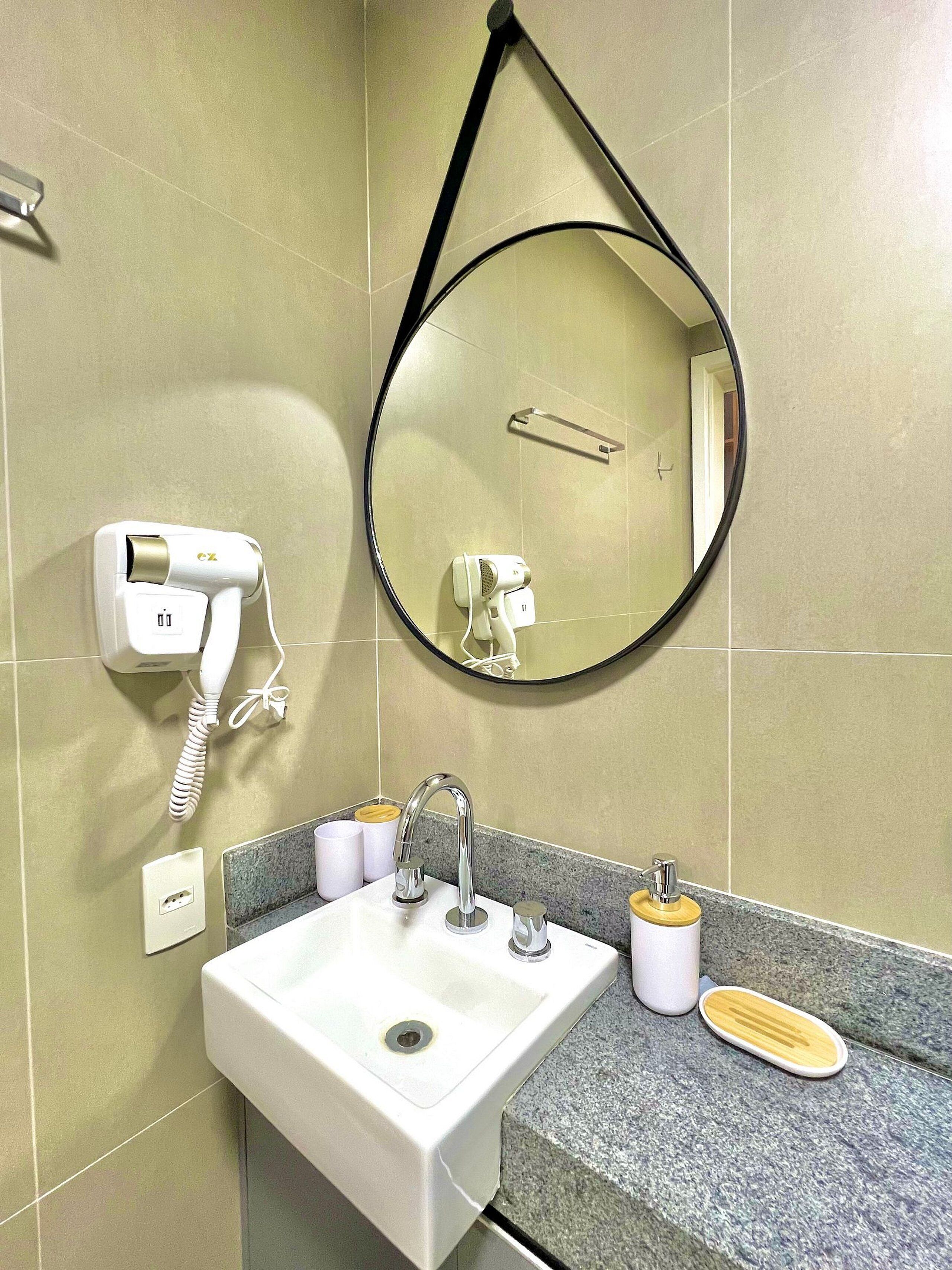 A bathroom with a sink, mirror, hairdryer, and towel rack.