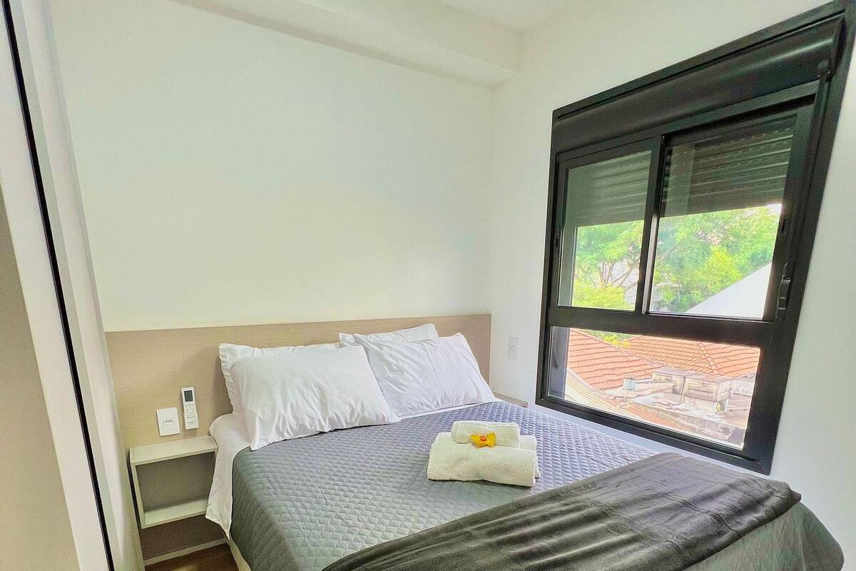 Un dormitorio con cama, mesita de noche, ventana con vista al exterior y puerta.