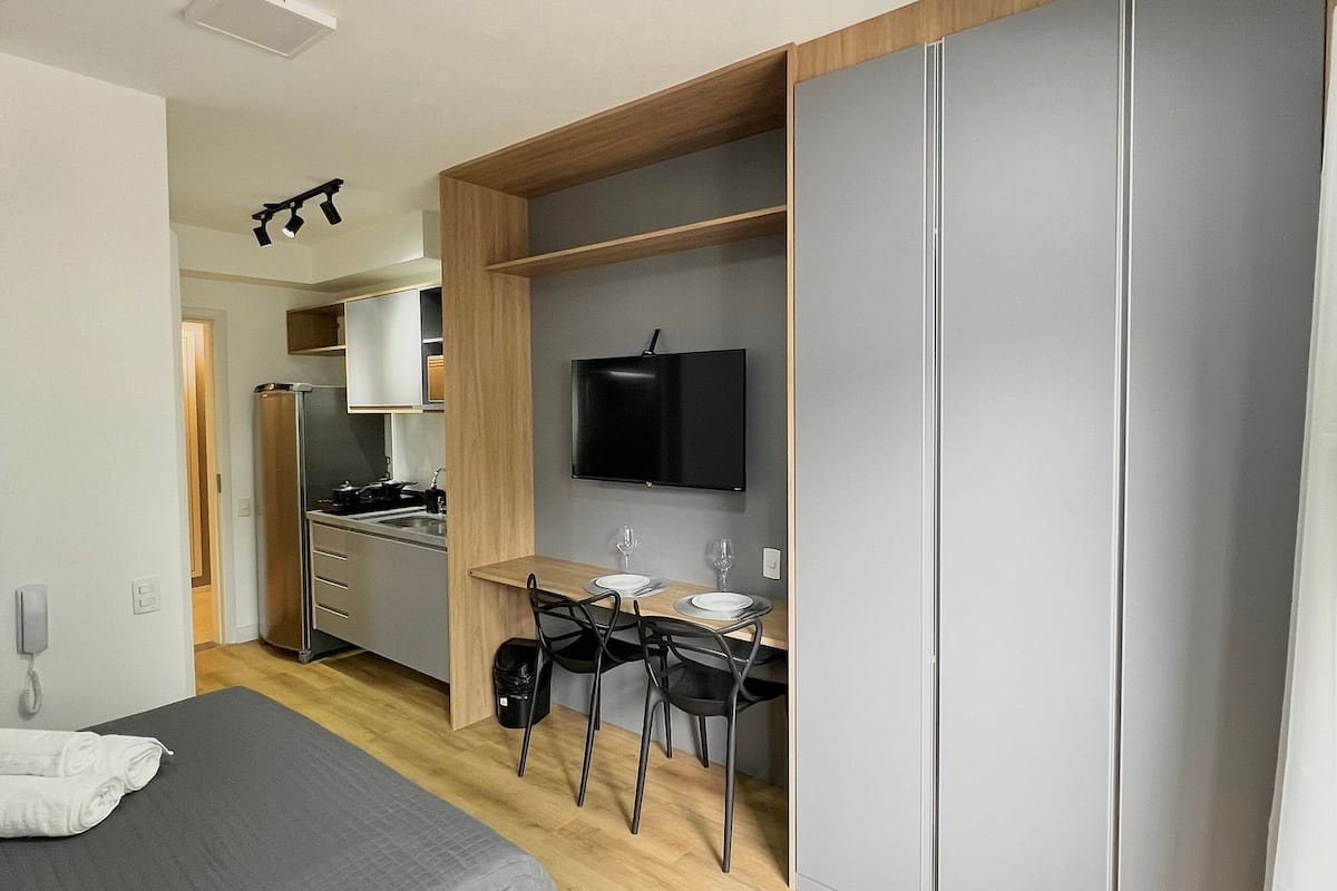 Una habitación de hotel moderna con una cama, un escritorio con sillas, un televisor y un armario.