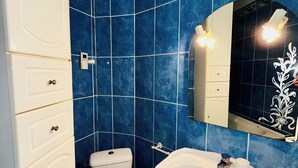 A bathroom with blue tiles, a white toilet, a white sink, and a mirror with a decorative frame. - Cosy and charming 2bed appartement in the Center PARIS marais (Paris)