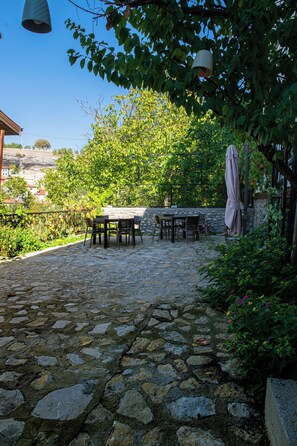 An outdoor patio with stone flooring, a table with chairs, and a pergola with a canopy.
