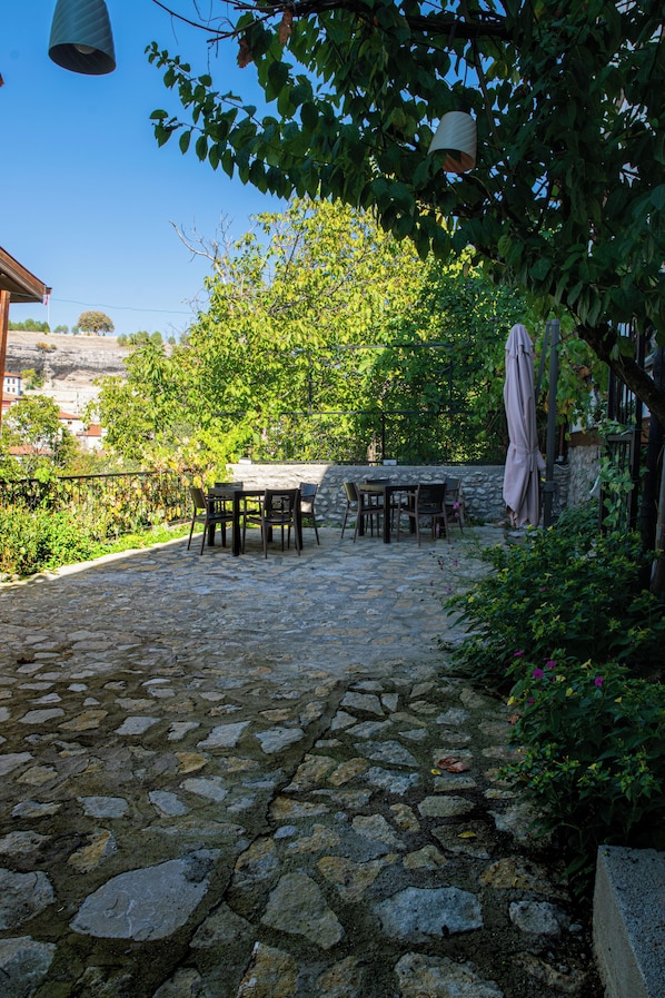 Une terrasse extérieure avec un sol en pierre, une table entourée de chaises et une pergola surmontée d’une toiture.
