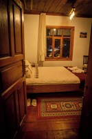 Un dormitorio con una cama de madera, una ventana con vistas a la ciudad de noche, una alfombra estampada y un armario de madera.