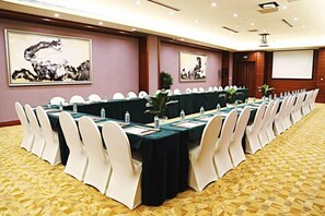 Un salón de conferencias con una larga mesa, sillas blancas y una pantalla para proyector.