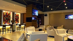 A modern lounge area with sofas and chairs, a bar with a colorful light display, and two TVs mounted on the wall. - Tiantai Yunjie International Hotel (Xiuwu)