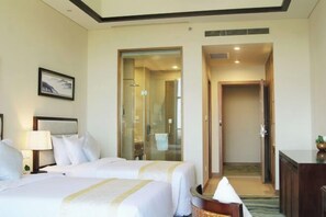 A hotel room with two beds, a desk, a lamp, a framed picture on the wall, and a bathroom visible through a glass door. - Tiantai Yunjie International Hotel (Xiuwu)