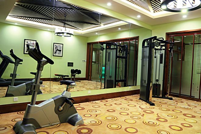 A gym with exercise equipment, a mirror, and a patterned carpet.