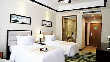 A hotel room with two beds, a ceiling fan, framed artwork on the walls, a wooden door, and a green patterned rug.