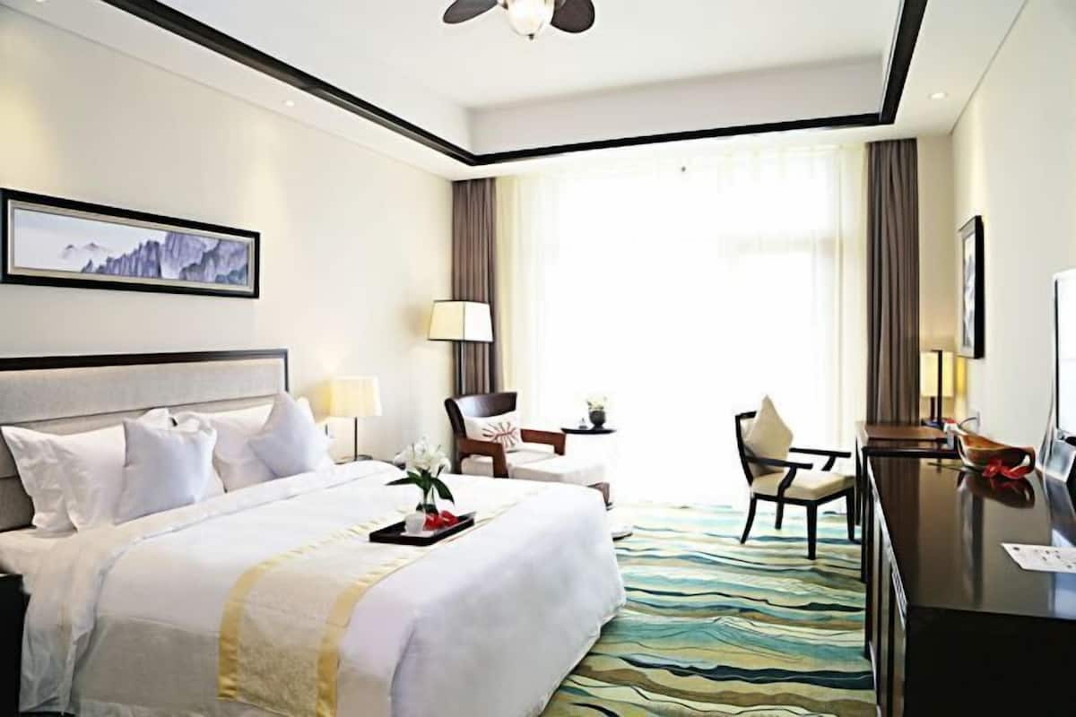 A hotel room with a bed, a desk, a chair, a lamp, a TV, and a painting on the wall.