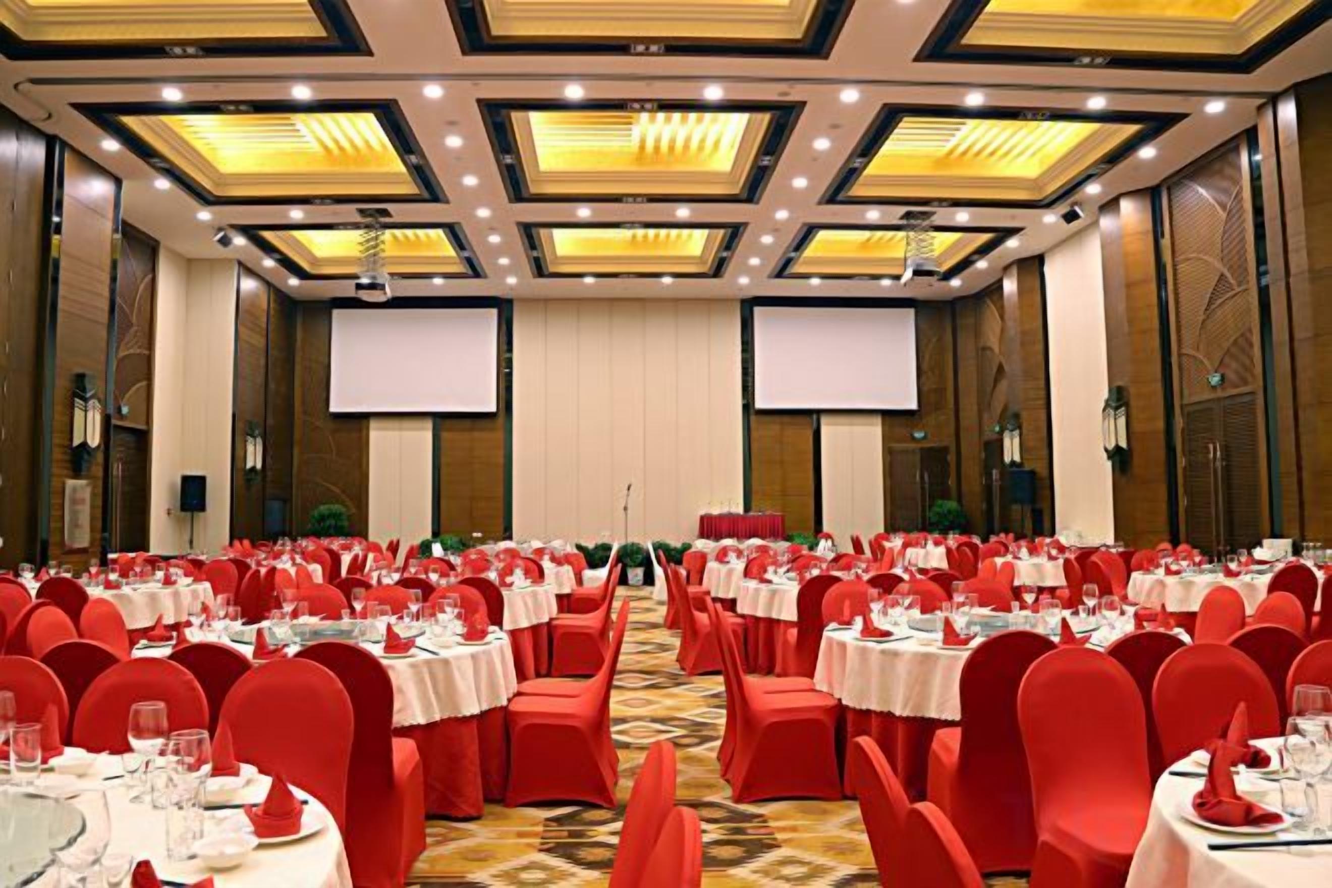A banquet hall with round tables, red chairs, and a carpeted floor.