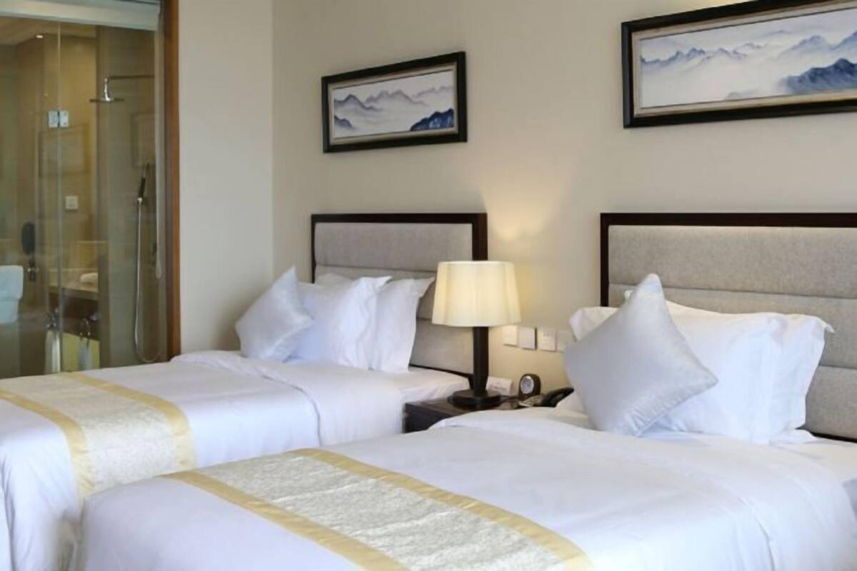 A hotel room with two beds, a glass shower enclosure, and two framed pictures on the wall.