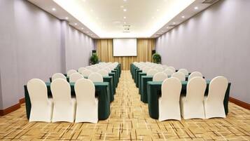A conference room with rows of tables and chairs, a projector screen, and a carpeted floor.