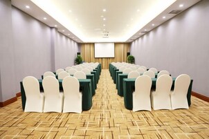 A conference room with rows of tables and chairs, a projector screen, and a carpeted floor.