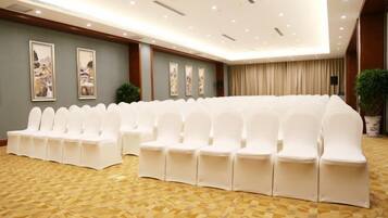 Un salón de conferencias con filas de sillas blancas, una alfombra estampada y cuadros en las paredes.