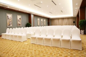 Un salón de conferencias con filas de sillas blancas, una alfombra estampada y cuadros en las paredes.