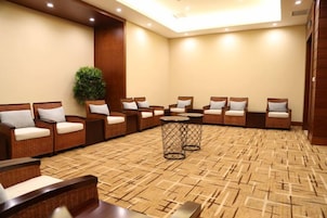 A room with a patterned carpet, several wicker sofas with cushions, a small round table, and a potted plant.