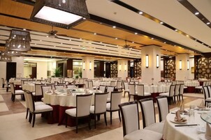 A banquet hall with multiple round tables, chairs, and a ceiling with recessed lighting.