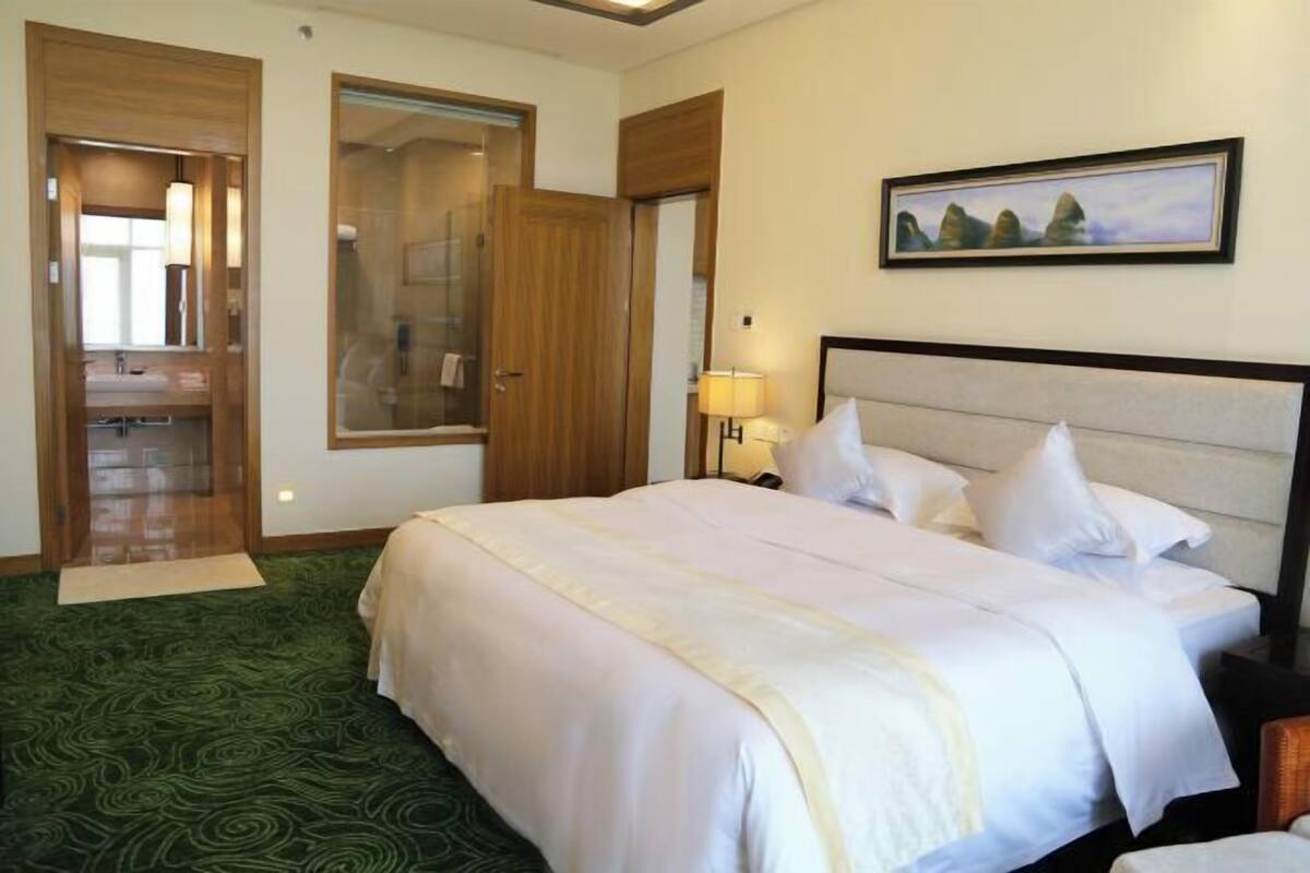 A hotel room with a large bed, a bathroom with a glass shower, and a painting on the wall.