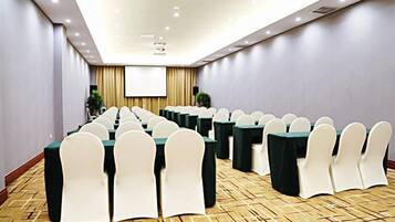 A conference room with rows of tables and chairs, a projector screen, and a carpeted floor.