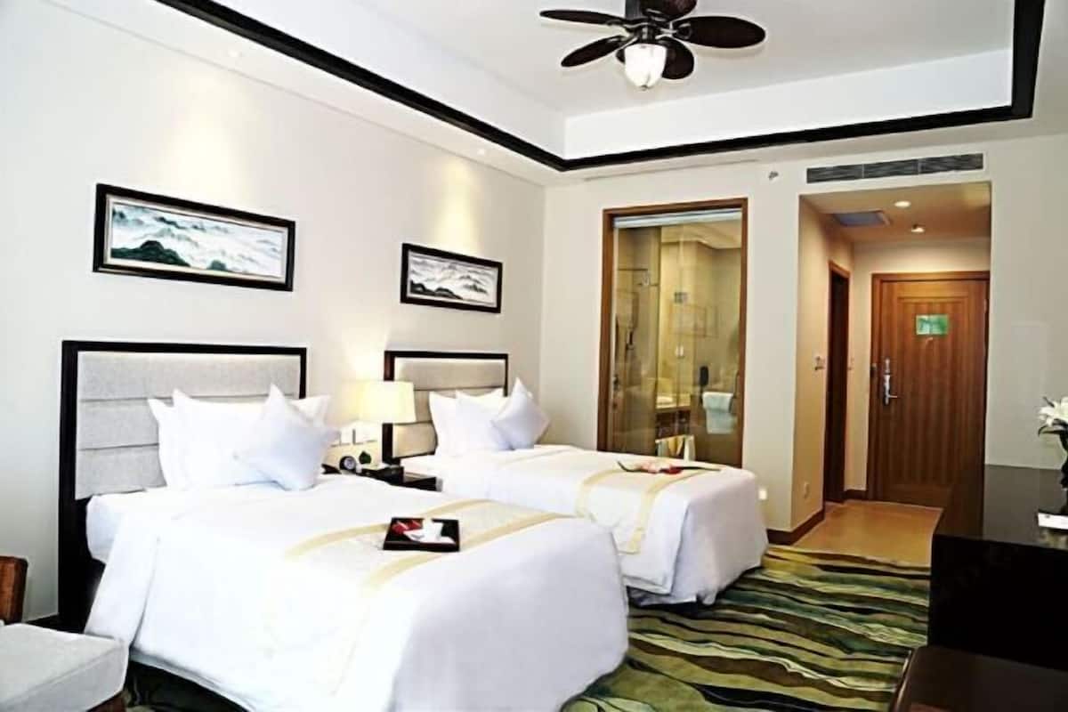 A hotel room with two beds, a ceiling fan, framed artwork on the walls, and a door leading to another room.