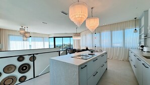 Une cuisine moderne dotée d’un îlot central, de luminaires suspendus et de grandes fenêtres.